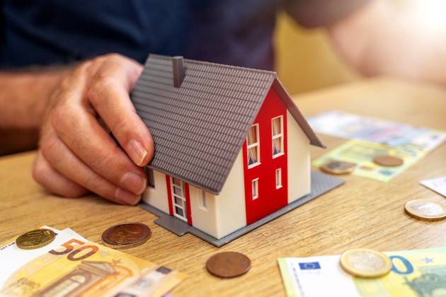 A house is held by an old man in his hand next to euro bills and coins. Real Estate and Finance Concept