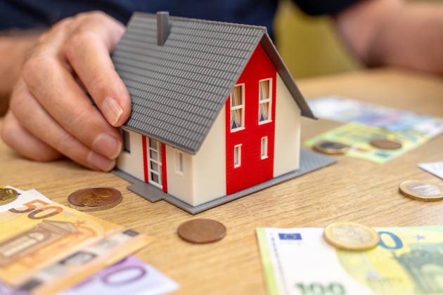 A house is held by an old man in his hand next to euro bills and coins. Real Estate and Finance Concept