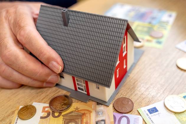 A house is held by an old man in his hand next to euro bills and coins. Real Estate and Finance Concept