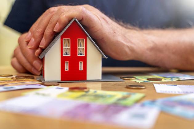 A house is held by an old man in his hand next to euro bills and coins. Real Estate and Finance Concept