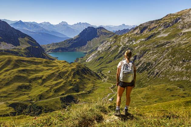 Eine junge Frau steht an einem Wanderweg auf einem Berg und schaut auf den Spullersee in Vorarlberg Lech Östereich