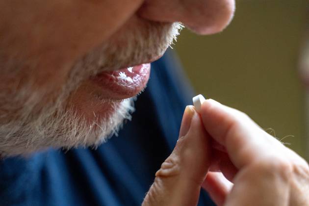 An old man takes a tablet with his mouth open. Disease and medicine concept
