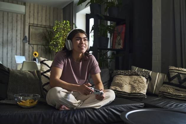 IMAGO Creative, Lifestyle, Gaming Happy young woman playing video game with controller on sofa at home model released, Symbolfoto property released, DSHF01146
