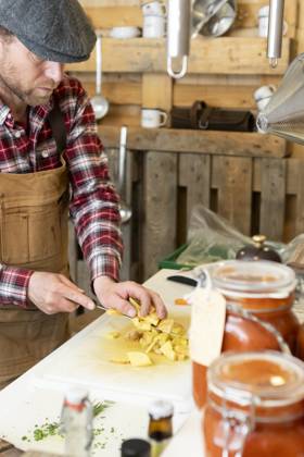 IMAGO Creative, Food, Trend, Meal Prep Crop focused chef in apron and beret standing in a rustic kitchen attentively dicing potatoes on a white cutting board with a background of hanging utensils and jars of homemade preserves Model Released JuanAizpuru_ID18273_546351_022 Copyright: xJuanxAizpurux