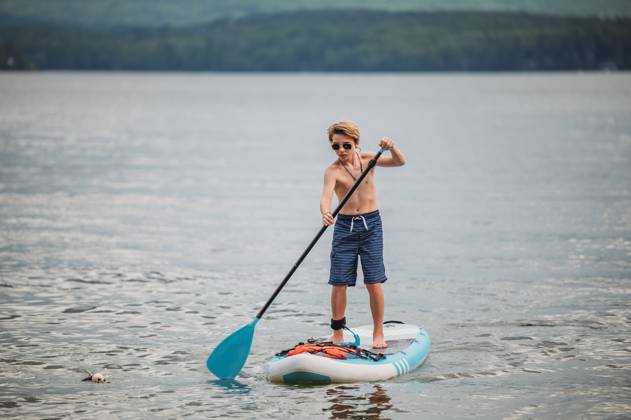 IMAGO Creative, Jahreszeit Sommer, Sommerferien Tween boy in sunglasses paddle boarding Wolfeboro, New Hampshire, United States R_ERBU231220-1310577-01 ,model released, Symbolfoto