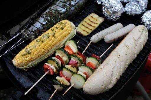 A high angle shot of seasoned vegetables on skewers, sausages, bread and stuffed fish cooking on grill 2386262