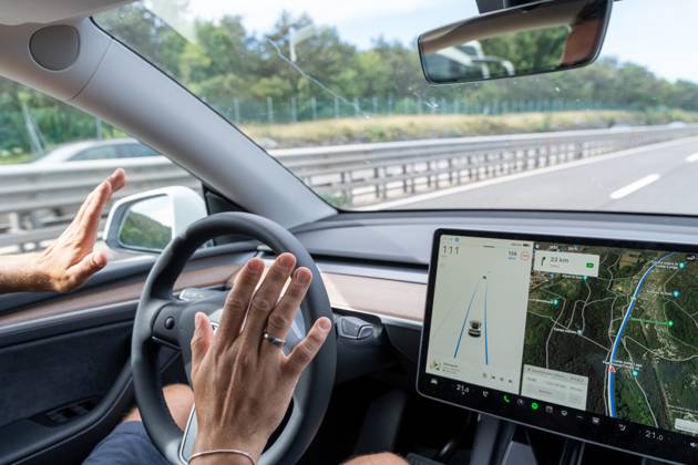 Mann fährt mit dem Tesla Model Y Auto auf der Autobahn mit Autopilot ohne Hände am Lenkrad