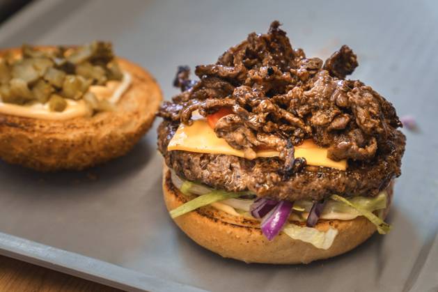 Zubereiteter Philly-Cheese-Burger auf einem Tablett in einem Imbiss mit frischem Rindfleisch, Tomate, Salat und geröstetem Hamburger Brötchen