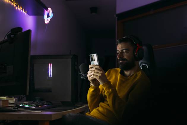 IMAGO Creative, Lifestyle, Gaming Influencer using smart phone near desktop PC at home model released, Symbolfoto property released, EGHF00828
