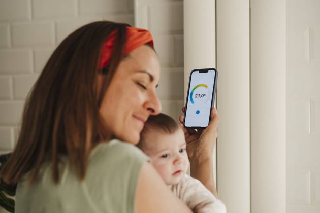 IMAGO Creative, Jahreszeit Sommer, Hitze Mother embracing baby daughter and adjusting radiator through smart phone at home model released, Symbolfoto property released, EBBF08730