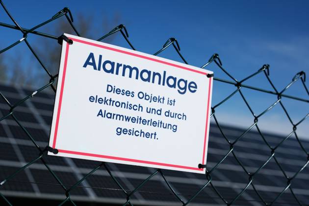 Hinweis auf Sicherung durch eine Alarmanlage am Zaun einer Solaranlage.