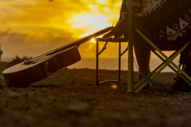 Back view of crop unrecognizable nomadic musician s guitar resting at a beachside campsite during a golden sunset, symbolizing inspiration and wanderlust. Model Released JuanAizpuru_ID20562_607331_033 Copyright: xJuanxAizpurux