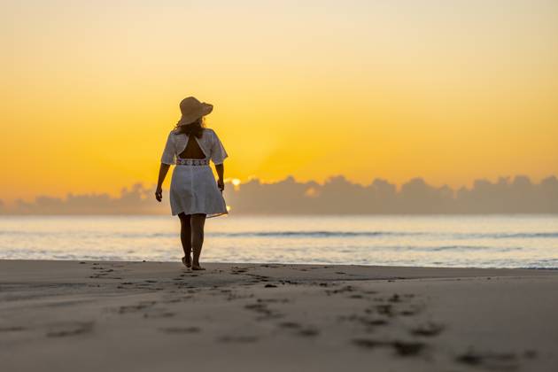 Back view of an unrecognizable woman enjoying a peaceful walk along the shore at sunrise, with the warm glow of the sun casting a tranquil backdrop. Model Released JuanAizpuru_ID20865_615527_019 Copyright: xJuanxAizpurux