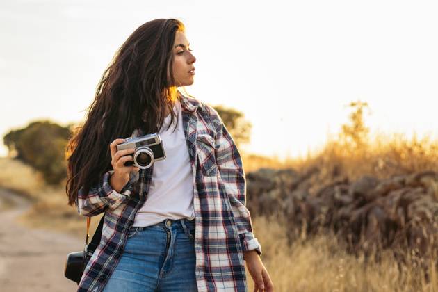 Young woman in checkered shirt and casual clothes taking photos with an analog camera in the field at sunset. The image conveys the concept of retro and vintage Model Released PedroMerino_ID19010_565605_021 Copyright: xx