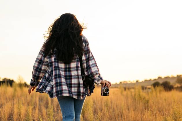 Young woman in checkered shirt and casual clothes taking photos with an analog camera in the field at sunset. The image conveys the concept of retro and vintage Model Released PedroMerino_ID19010_565607_023 Copyright: xx