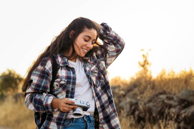 Young woman in checkered shirt and casual clothes taking photos with an analog camera in the field at sunset. The image conveys the concept of retro and vintage Model Released PedroMerino_ID19010_565619_029 Copyright: xx