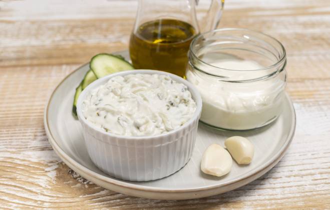 Traditional greek yogurt sauce Tzatziki,dressing in white bowl, made of grated cucumbers, sour cream yogurt,olive oil,garlic,herbs with ingredients on wooden table. Close up, horizontal Traditional greek yogurt sauce Tzatziki in white bowl, made of chopped cucumbers, sour cream yogurt,olive oil,garlic,herbs with ingredients on wooden table. Rustic style. Close up, horizontal plane. Copyright: x