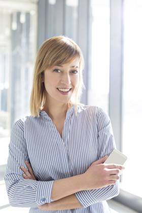 Portrait of smiling businesswoman holding mobile phone while standing at office ,model released, Symbolfoto