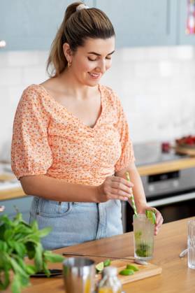 culinary and people concept - happy smiling young woman making cocktail drinks with lime and peppermint at home kitchen. woman making cocktail drinks at home kitchen ,model released, Symbolfoto