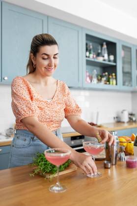 culinary and people concept - happy smiling young woman making cocktail drinks at home kitchen. woman making cocktail drinks at home kitchen ,model released, Symbolfoto