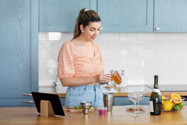 culinary and people concept - happy smiling young woman with tablet pc computer making cocktail drinks at home kitchen. woman with tablet pc making cocktails at kitchen ,model released, Symbolfoto