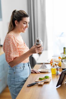 culinary and people concept - happy smiling young woman with tablet pc computer making cocktail drinks at home kitchen. woman with tablet pc making cocktails at kitchen ,model released, Symbolfoto