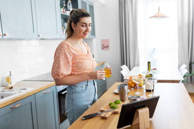culinary and people concept - happy smiling young woman with tablet pc computer making cocktail drinks at home kitchen. woman with tablet pc making cocktails at kitchen ,model released, Symbolfoto