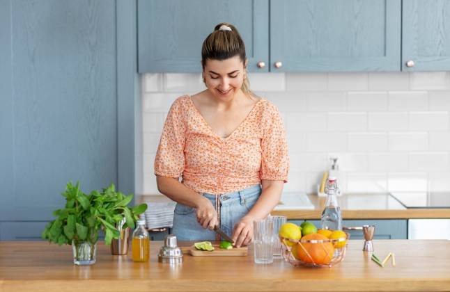 culinary and people concept - happy smiling young woman making cocktail drinks with lime and peppermint at home kitchen. woman making cocktail drinks at home kitchen ,model released, Symbolfoto