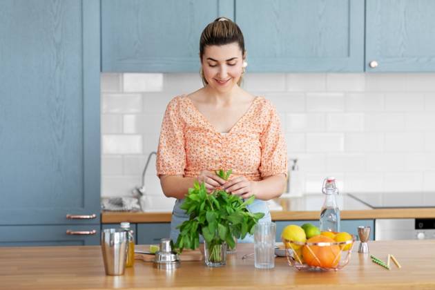 culinary and people concept - happy smiling young woman making cocktail drinks with lime and peppermint at home kitchen. woman making cocktail drinks at home kitchen ,model released, Symbolfoto