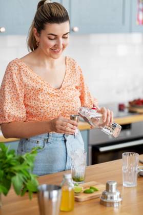 culinary and people concept - happy smiling young woman making cocktail drinks at home kitchen. woman making cocktail drinks at home kitchen ,model released, Symbolfoto