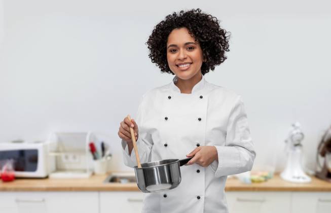 culinary and people concept - happy smiling female chef in jacket with saucepan cooking food over restaurant kitchen background. happy smiling female chef with saucepan on kitchen ,model released, Symbolfoto