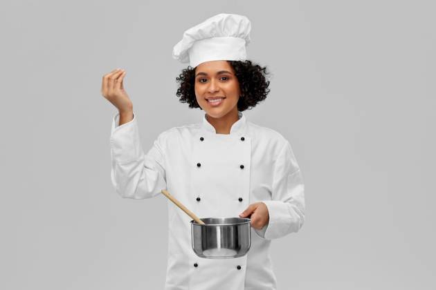 culinary and people concept - happy smiling female chef in toque with saucepan cooking food showing gourmet sign over grey background. female chef with saucepan and spoon cooking food ,model released, Symbolfoto