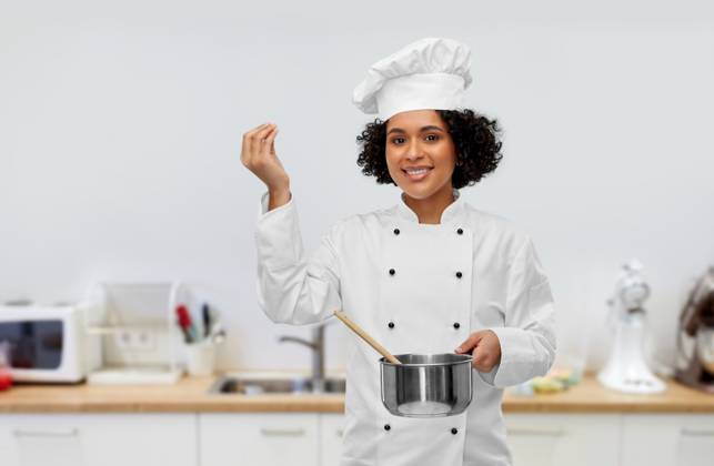 culinary and people concept - happy smiling female chef in toque with saucepan cooking food showing gourmet sign over kitchen background. female chef with saucepan and spoon cooking food ,model released, Symbolfoto