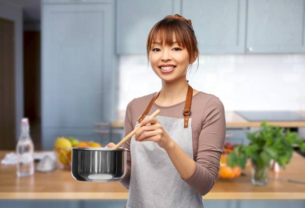 culinary and people concept - happy smiling female chef in jacket with saucepan cooking food over home kitchen background. happy smiling female chef with saucepan in kitchen ,model released, Symbolfoto