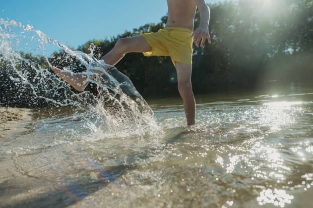 Playful boy kicking and splashing water at river on sunny day model released, Symbolfoto, ANAF03623