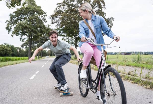 Cheerful man skateboarding with girlfriend riding bicycle on road model released, Symbolfoto, UUF32646