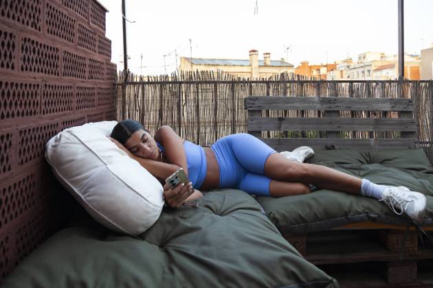 Creative Highlights Symbolfotos Woman lies comfortably on outdoor bed while operating her smartphone at sunrise in Barcelona, looking at the screen Model Released Almuzambrana_ID23844_692095_008 Copyright: xAlmuzambranax