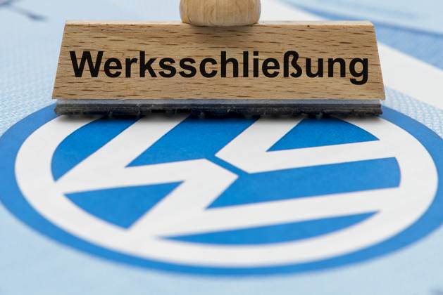 VW-Krise mit Gefahr der Werksschließung Ein Holzstempel ist beschriftet mit dem Aufdruck: Werksschließung, über einer VW-Aktie mit Logo - Symbolbild