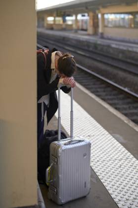 IMAGO Creative, Gesellschaft, Leisure Sickness Exhausted traveler resting on a suitcase at a train station platform. bola04432 Copyright: xConnectxImagesx ,model released