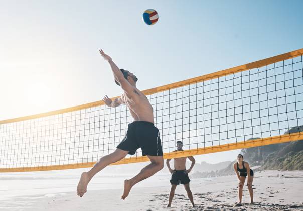 Man, jump and volleyball in air on beach by net in sports match, game or competition. Body of male person jumping for ball in volley or spike in healthy fitness, energy or exercise by the ocean coast. model released property released Copyright: xwww.peopleimages.comx
