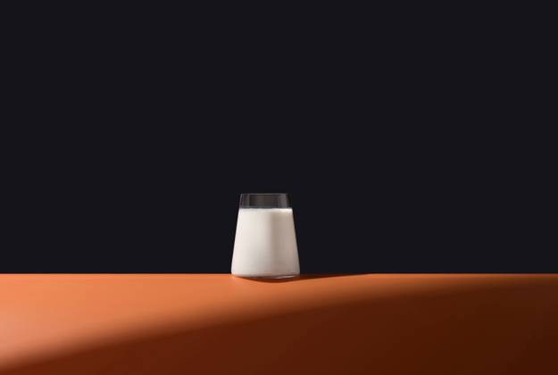 A simple and elegant image featuring a full glass of milk on a vibrant orange surface, set against a dark, contrasting background Ideal for showcasing purity and freshness Model Released RuthCarrodeguas_ID24758_717745_001 Copyright: xRuthxCarrodeguasx RECORD DATE NOT STATED