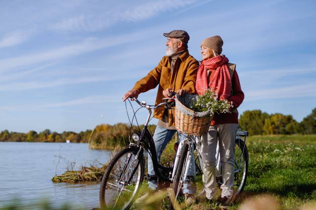 Lovely elderly couple on standing by lake with their bikes, enjoying a peaceful moment together. Lovely elderly couple on standing by lake with their bikes, enjoying peaceful moment together. model released