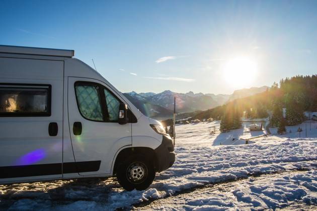Ein Camper steht im Winter auf einem Parkplatz in den Alpen bei Sonnenaufgang im Schnee. Bödele, Vorarlberg, Österreich Winter in den österreichischen Alpen