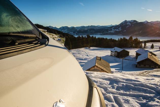 Ein Camper steht im Winter auf einem Parkplatz in den Alpen bei Sonnenaufgang im Schnee. Bödele, Vorarlberg, Österreich Winter in den österreichischen Alpen