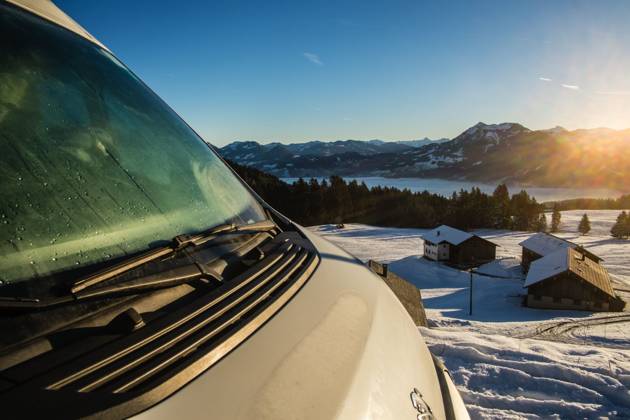 Ein Camper steht im Winter auf einem Parkplatz in den Alpen bei Sonnenaufgang im Schnee. Bödele, Vorarlberg, Österreich Winter in den österreichischen Alpen