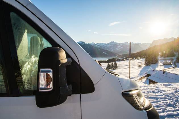 Ein Camper steht im Winter auf einem Parkplatz in den Alpen bei Sonnenaufgang im Schnee. Bödele, Vorarlberg, Österreich Winter in den österreichischen Alpen
