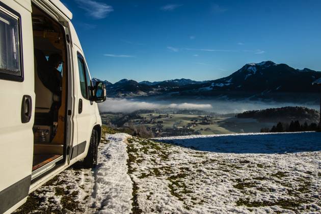 Ein Camper steht im Winter auf einem Parkplatz in den Alpen bei Sonnenaufgang im Schnee. Bödele, Vorarlberg, Österreich Winter in den österreichischen Alpen