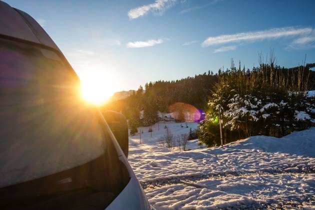 Ein Camper steht im Winter auf einem Parkplatz in den Alpen bei Sonnenaufgang im Schnee. Bödele, Vorarlberg, Österreich Winter in den österreichischen Alpen
