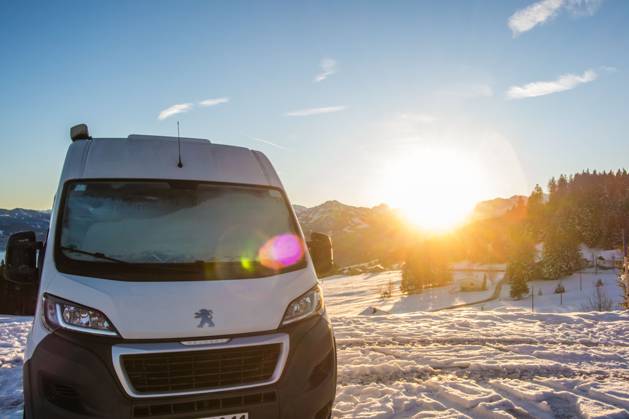 Ein Camper steht im Winter auf einem Parkplatz in den Alpen bei Sonnenaufgang im Schnee. Bödele, Vorarlberg, Österreich Winter in den österreichischen Alpen