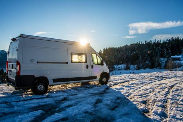 Ein Camper steht im Winter auf einem Parkplatz in den Alpen bei Sonnenaufgang im Schnee. Bödele, Vorarlberg, Österreich Winter in den österreichischen Alpen